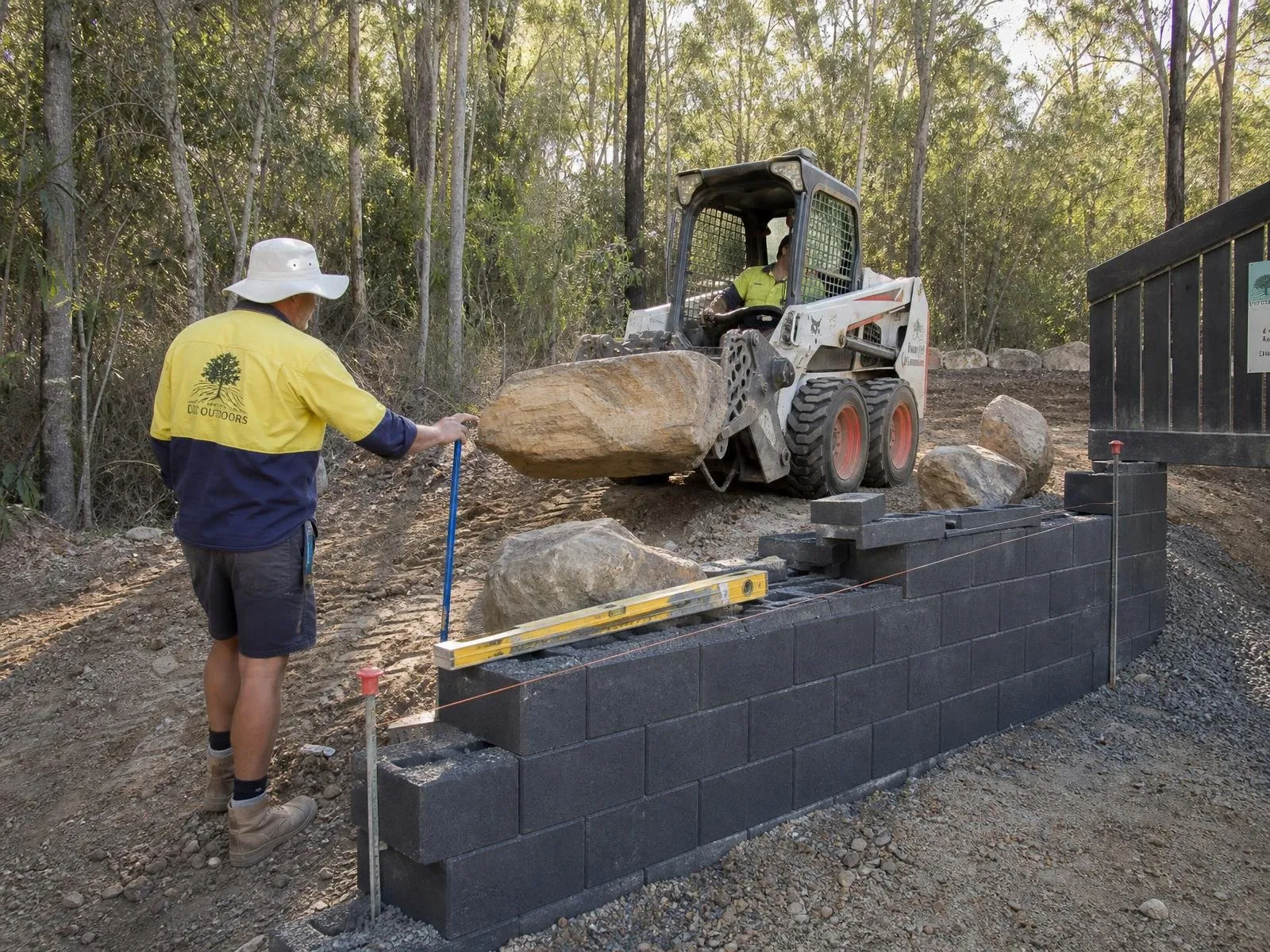 Australian landscape construction site with skid-steer loader and sandstone boulders being placed