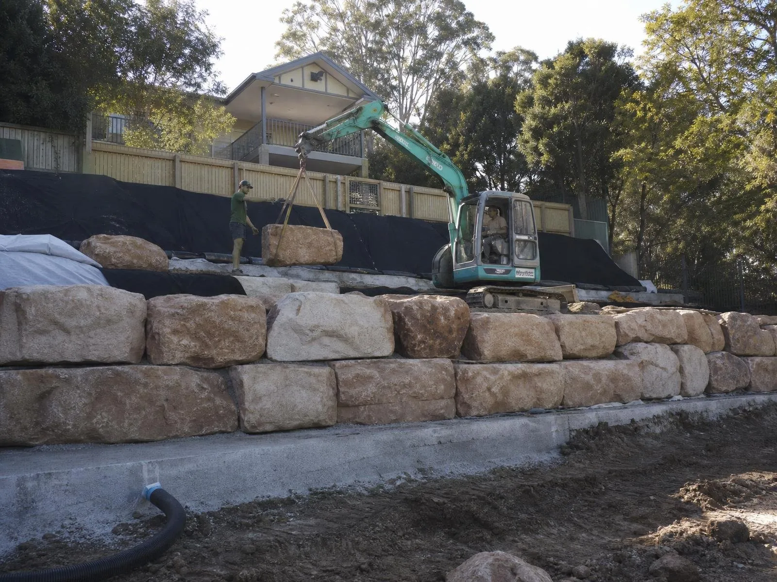 Australian structural landscape works with excavator placing sandstone blocks on a retaining wall